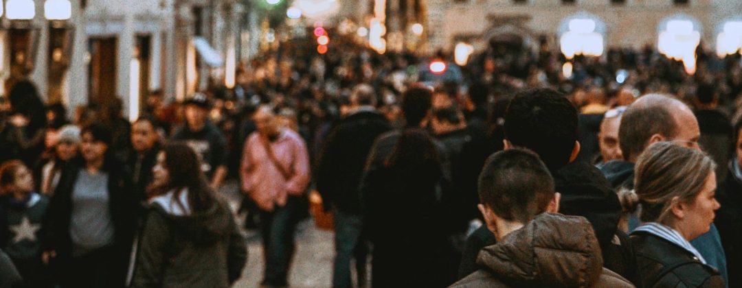 A vibrant street filled with people in the evening, showcasing urban life and city architecture.