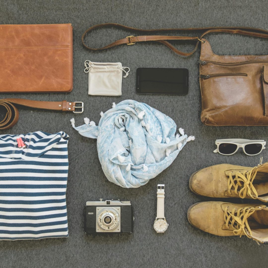 Vintage travel essentials flat lay with leather bags, shoes, camera, and clothing.